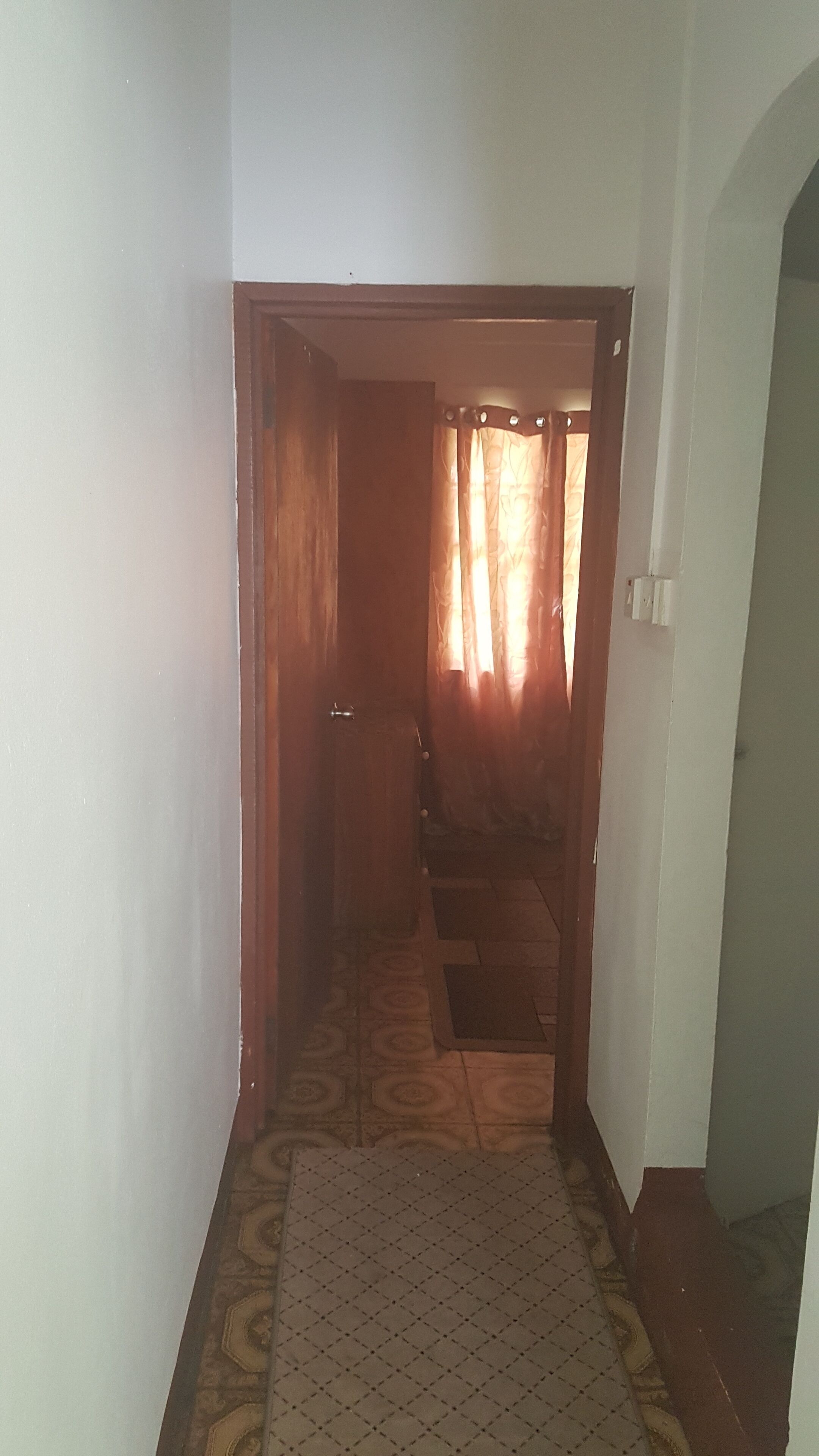 A narrow hallway with patterned floor tiles, a wooden door, and a curtain.