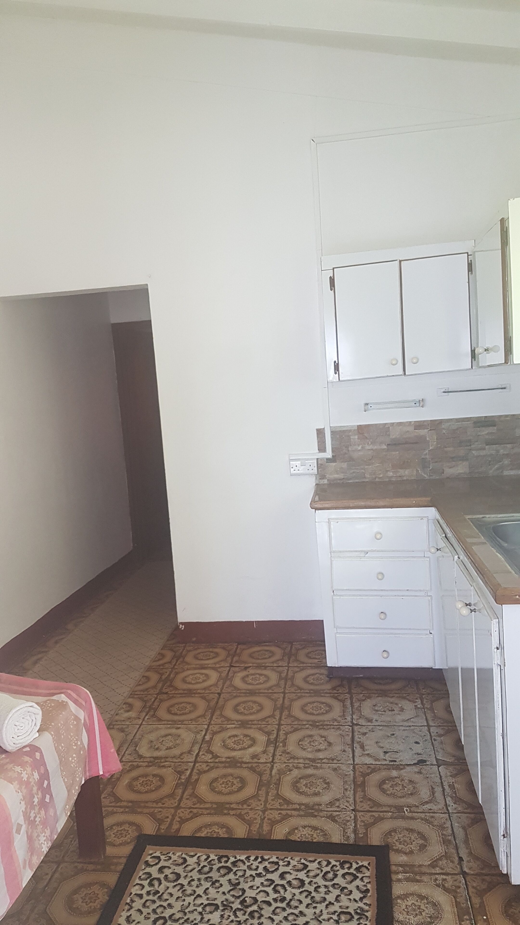 A compact kitchen with white cabinets, a countertop, and a patterned floor.