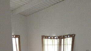 A bedroom with a bed, curtains, and a rug. - Honiiwell rooms and suites (St. George's)