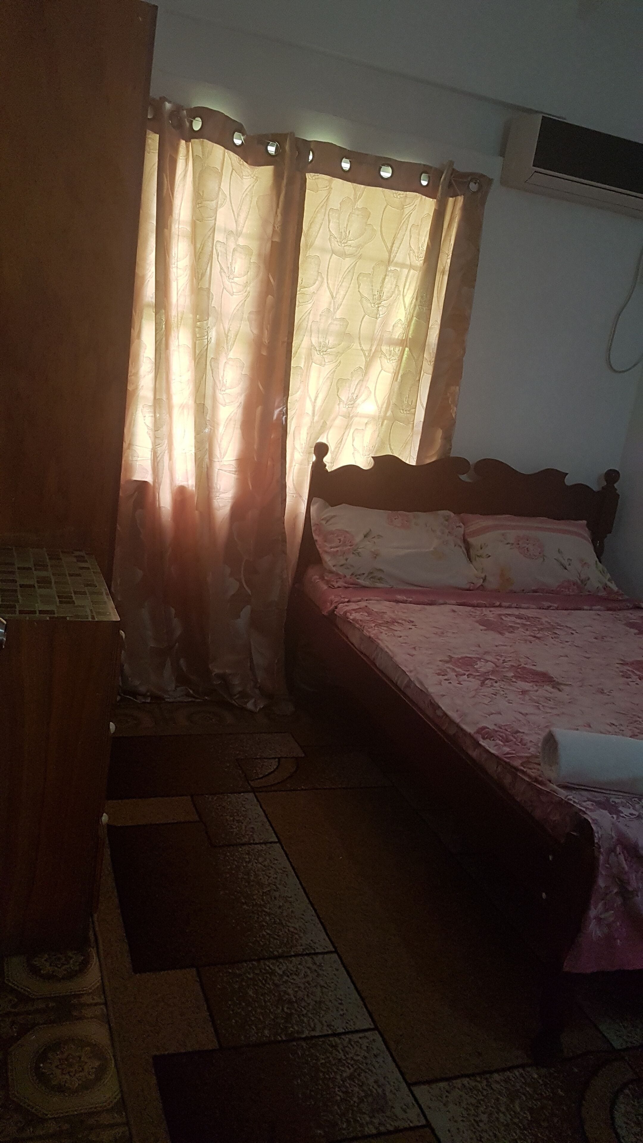 A bedroom with a bed, curtains, an air conditioning unit, and a patterned rug.