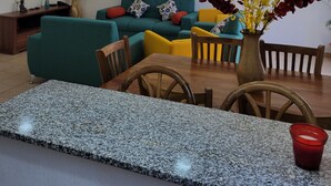 Un salon moderne avec un canapé vert, des chaises en bois, une table en granit et un vase rempli de fleurs.