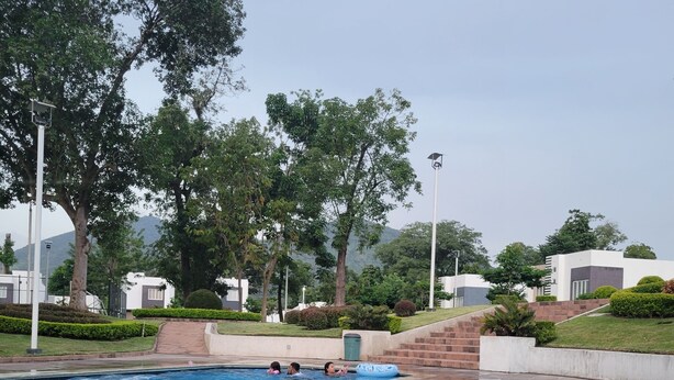 Une piscine dotée d’une terrasse carrelée, entourée de verdure et de bâtiments modernes.