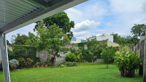Un patio abrité avec une pelouse verdoyante, des plantes en pot et une vue sur un quartier résidentiel.