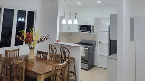 Une cuisine moderne avec des armoires blanches, une cuisinière à gaz et un four à micro-ondes. On y trouve un coin repas avec des chaises et une table en bois, ainsi qu’un vase rempli de fleurs posé sur la table.