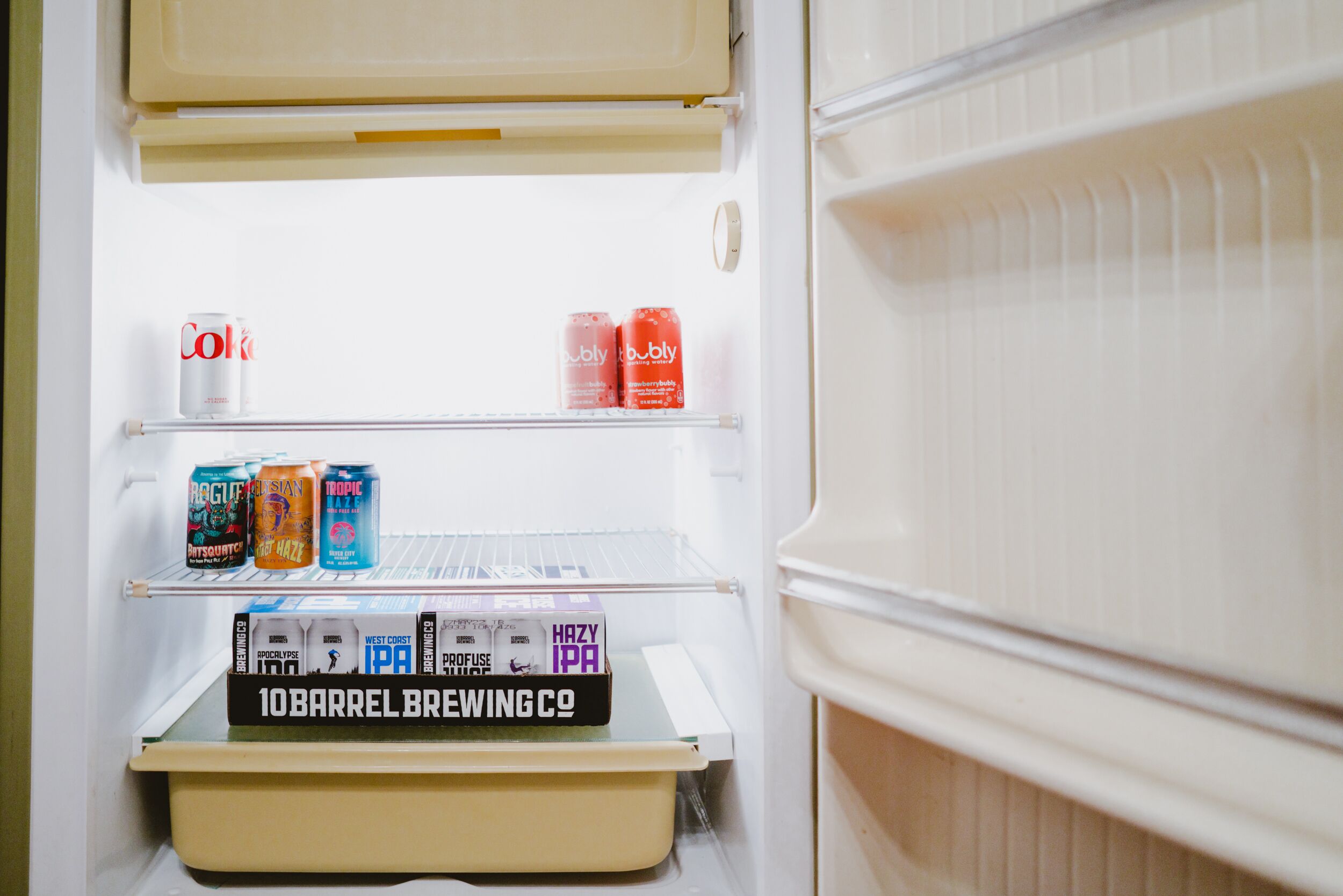 Ein Kühlschrank mit Regalen, auf denen verschiedene Getränke und eine Kiste mit dem Aufdruck '10 Barrel Brewing Co.' stehen.