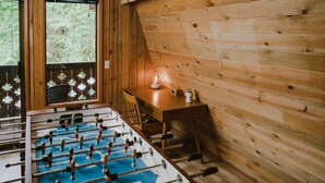 Una stanza con pavimento in legno, un tavolo da calcio e una finestra vista alberi.