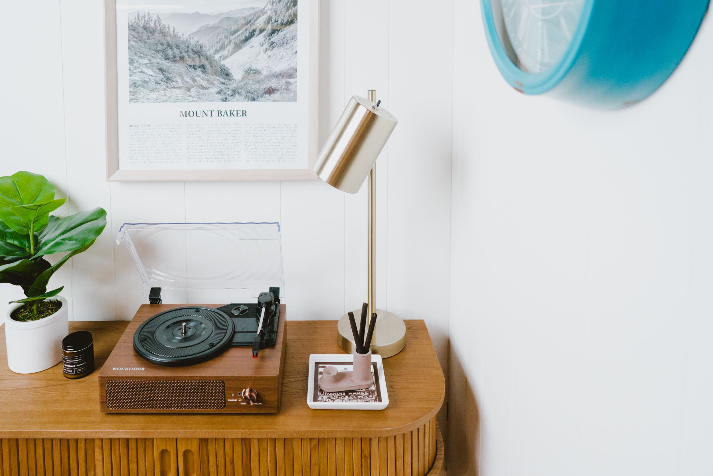 A wooden desk with a turntable, a framed picture of Mount Baker, a lamp, and a potted plant.
