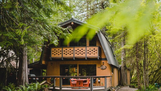 Una baita di legno a due piani con un balcone, immersa in una fitta foresta.