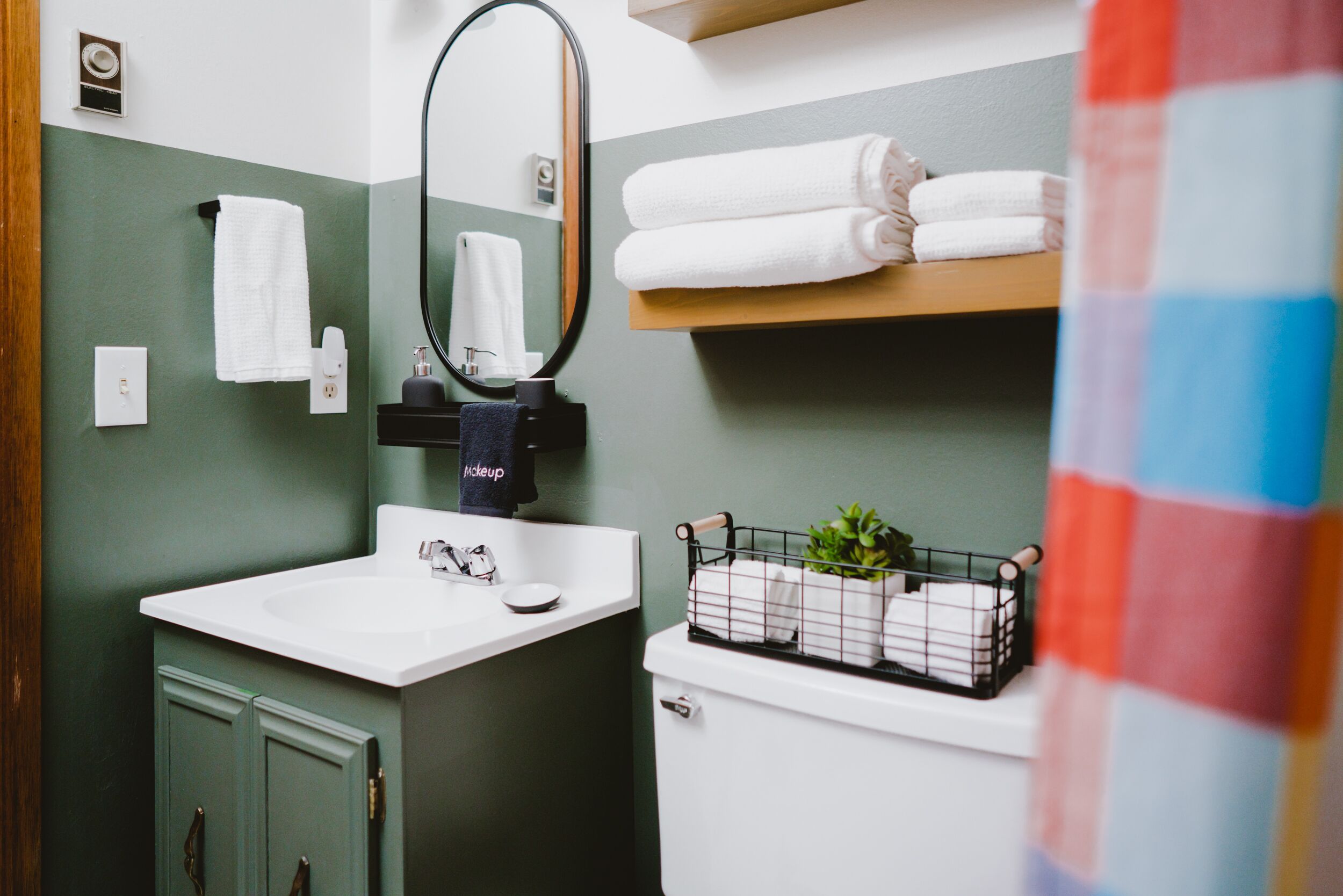 A bathroom with a white sink, green cabinets, a mirror, and a shelf with folded towels.