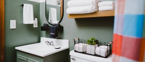 A bathroom with a white sink, green cabinets, a mirror, and a shelf with folded towels.