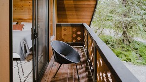 Un balcone in legno con una sedia, un letto con coperta e una porta che dà su una stanza.