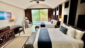 Habitación de hotel con una cama grande, un escritorio, una silla, un televisor y un balcón con vistas a palmeras.