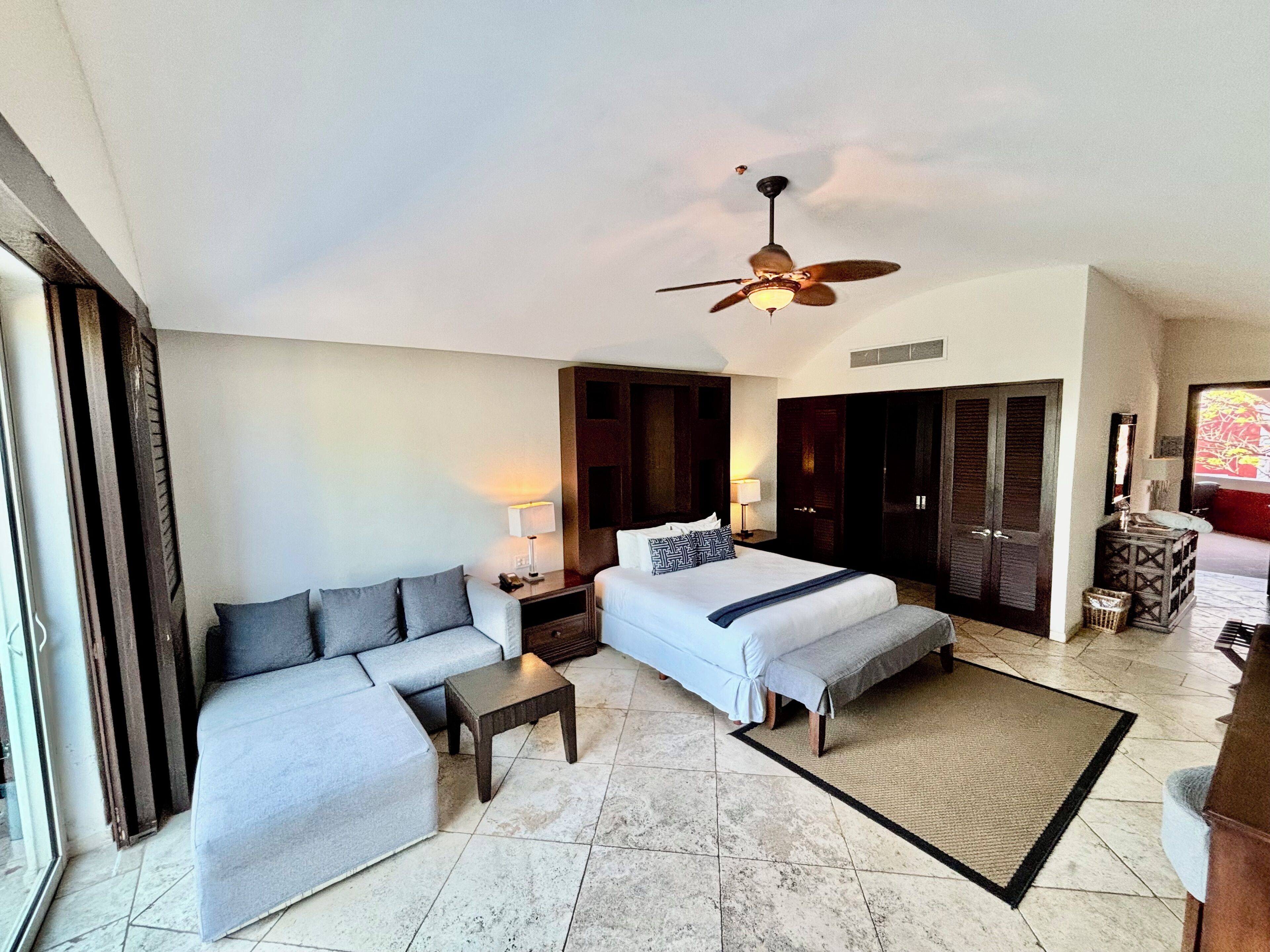 Ein Hotelzimmer mit Bett, Sofa, kleinem Tisch, Deckenventilator und Blick ins Freie.
