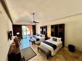Habitación de hotel con dos camas, un escritorio y una silla. Cuenta con ventilador de techo, televisión y ventana con vistas al exterior.