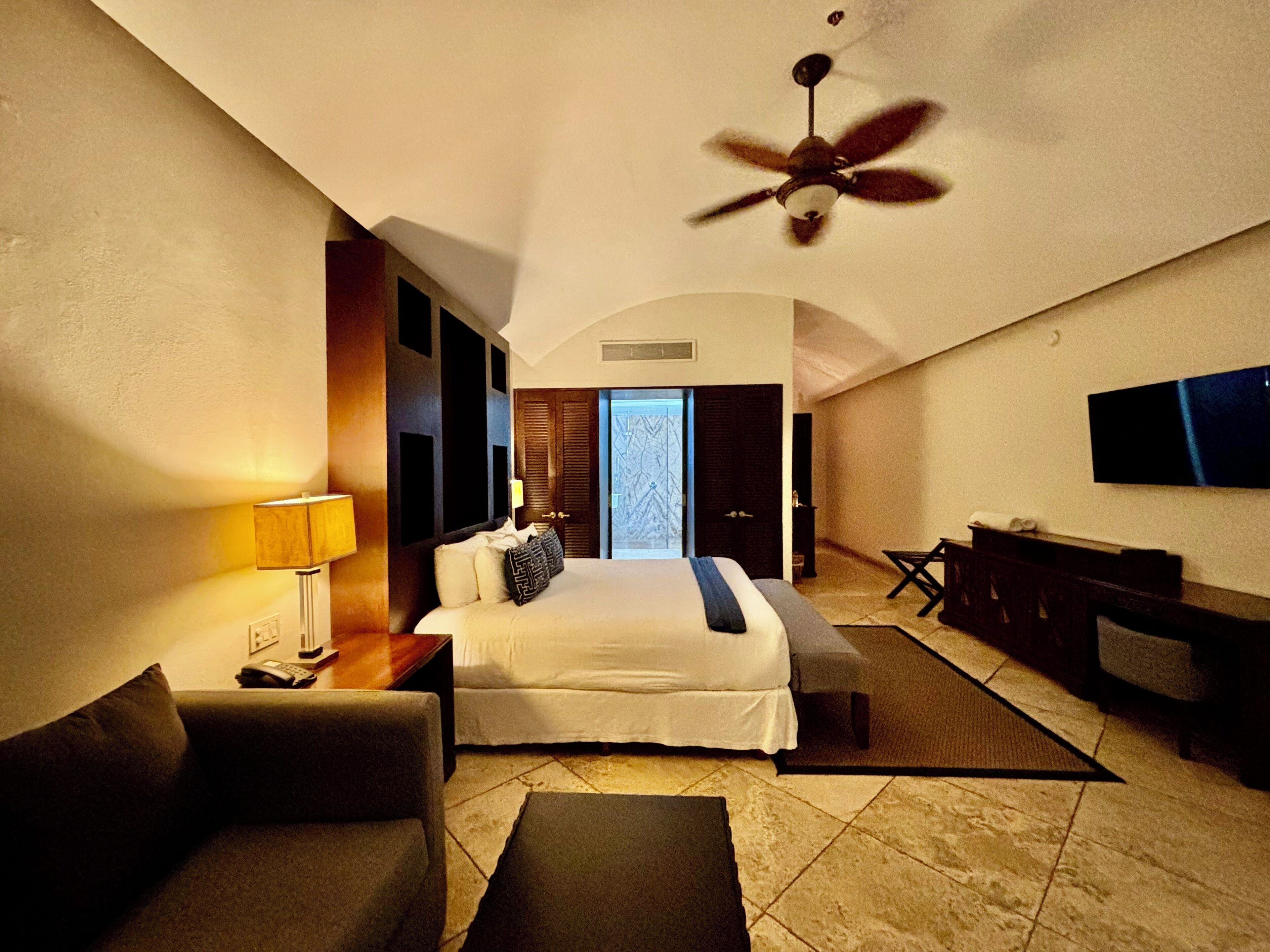 A hotel room with a bed, a desk, a TV, and a ceiling fan.