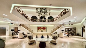 Amplia sala de estar con una mesa redonda central, varias opciones de asiento, una escalera y un cuadro grande en la pared.