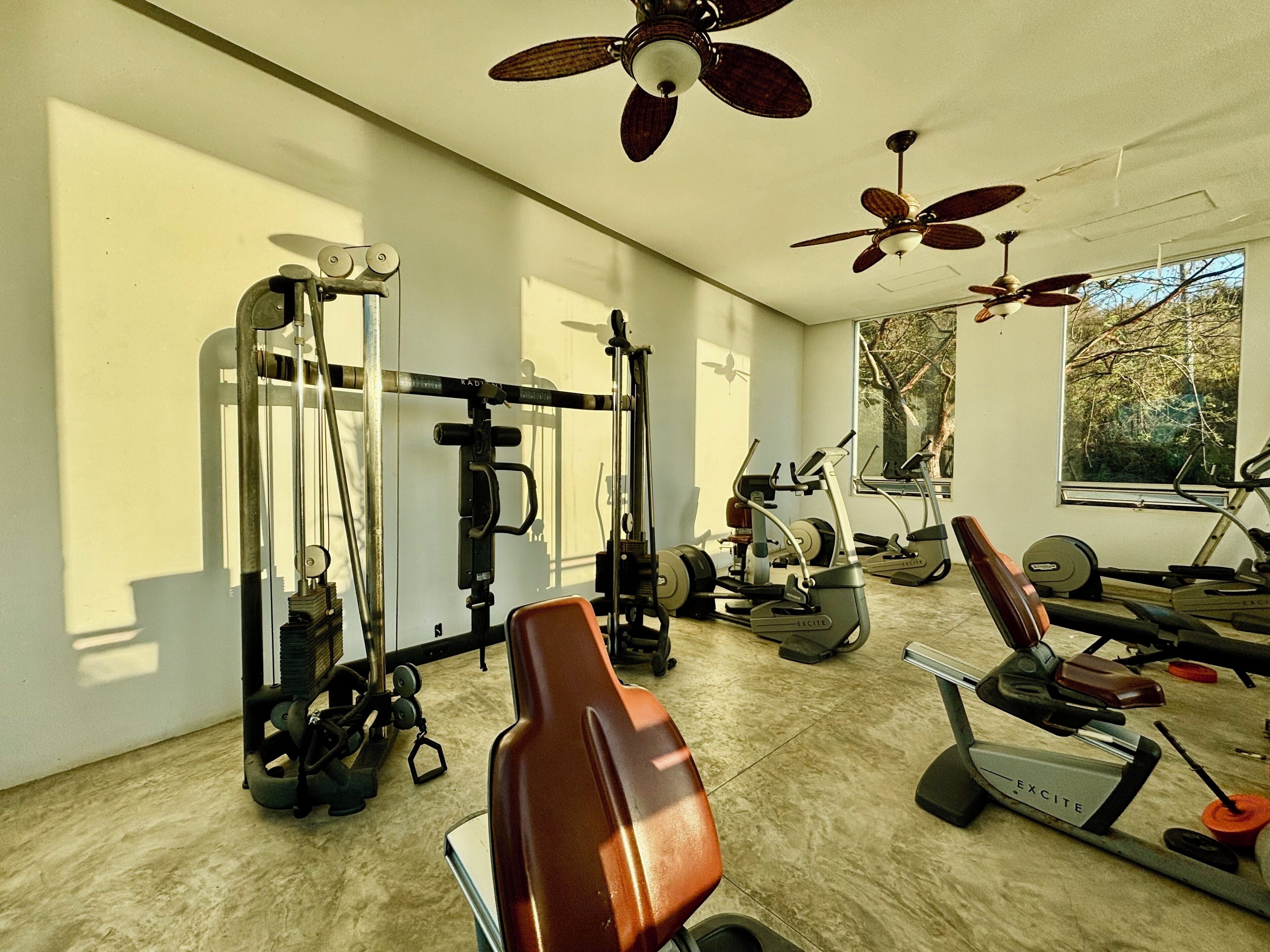Un gimnasio con ventiladores de techo, equipo de ejercicio y un ventanal grande.