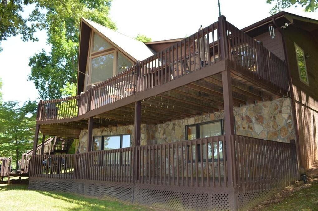 Eine zweistöckige Holzhütte mit Balkon, Steinmauern und einer überdachten Terrasse.