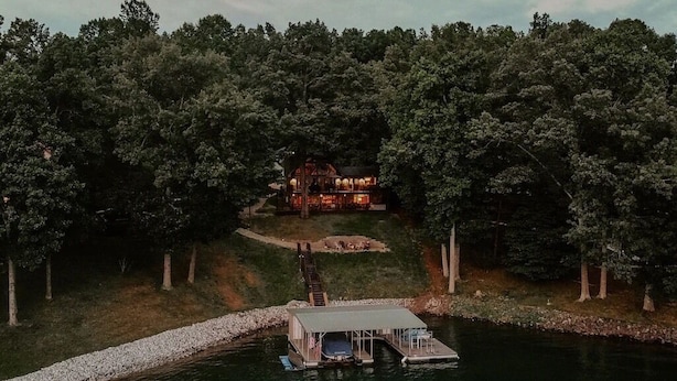 Una cabaña junto al lago con un muelle y un bote, rodeada de un bosque denso.