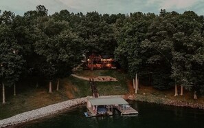 Una cabaña junto al lago con un muelle y un bote, rodeada de un bosque denso.