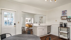 A modern kitchen with white cabinetry, a dining area with a round table, and a coffee station.