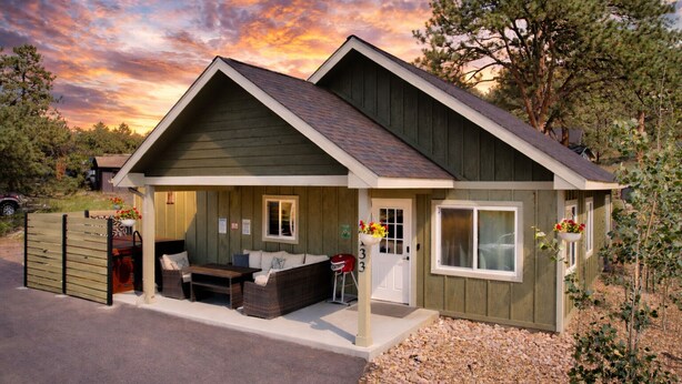 A small, single-story house with a porch, a covered outdoor seating area, and a number '133' on the door. - Hike Into RMNP From House-Coaster Passes-Hot Tub-King Bed-A/C-BBQ (Estes Park)