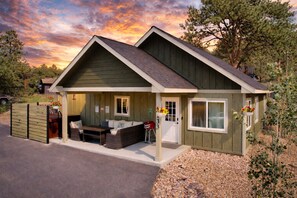 A small, single-story house with a porch, a covered outdoor seating area, and a number '133' on the door. - Hike Into RMNP From House-Coaster Passes-Hot Tub-King Bed-A/C-BBQ (Estes Park)