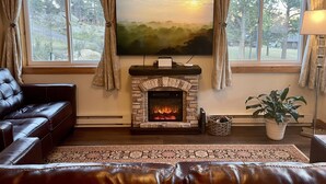 A cozy living room with a fireplace, leather sofa, and a large window with curtains. - Hike Into RMNP From House-Coaster Passes-Hot Tub-King Bed-A/C-BBQ (Estes Park)