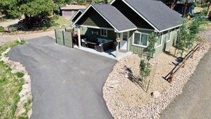 A two-story house with a covered porch, a driveway, and a small garden area. - Hike Into RMNP From House-Coaster Passes-Hot Tub-King Bed-A/C-BBQ (Estes Park)