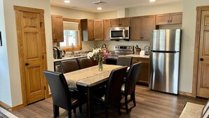 A modern kitchen with wooden cabinets, stainless steel appliances, and a dining area with a table and chairs. - Hike Into RMNP From House-Coaster Passes-Hot Tub-King Bed-A/C-BBQ (Estes Park)