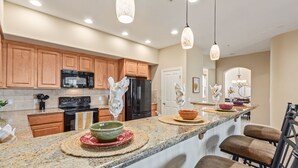 A modern kitchen with granite countertops, wooden cabinets, stainless steel appliances, and a central island with bar seating. - Serenity Town House! Heated Pool, Gym! 2 King Beds! 1 Dog Friendly! (Chandler)