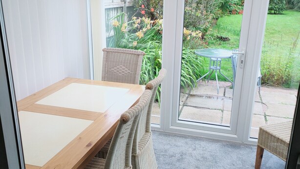 Une véranda avec une table en bois et des chaises en osier, une porte vitrée donnant sur un jardin.