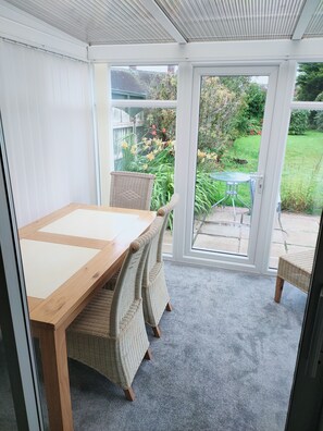 A conservatory with a wooden table and wicker chairs, a glass door leading to a garden. - Charming 2-Bed House in Fleetwood, England (Fleetwood)