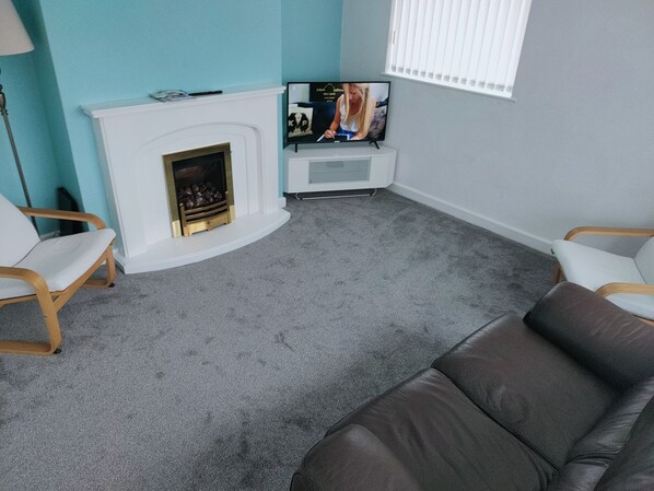 A living room with a fireplace, a television, and two chairs. - Charming 2-Bed House in Fleetwood, England (Fleetwood)
