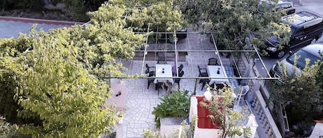 An outdoor seating area with tables and chairs, surrounded by trees and a stone wall.