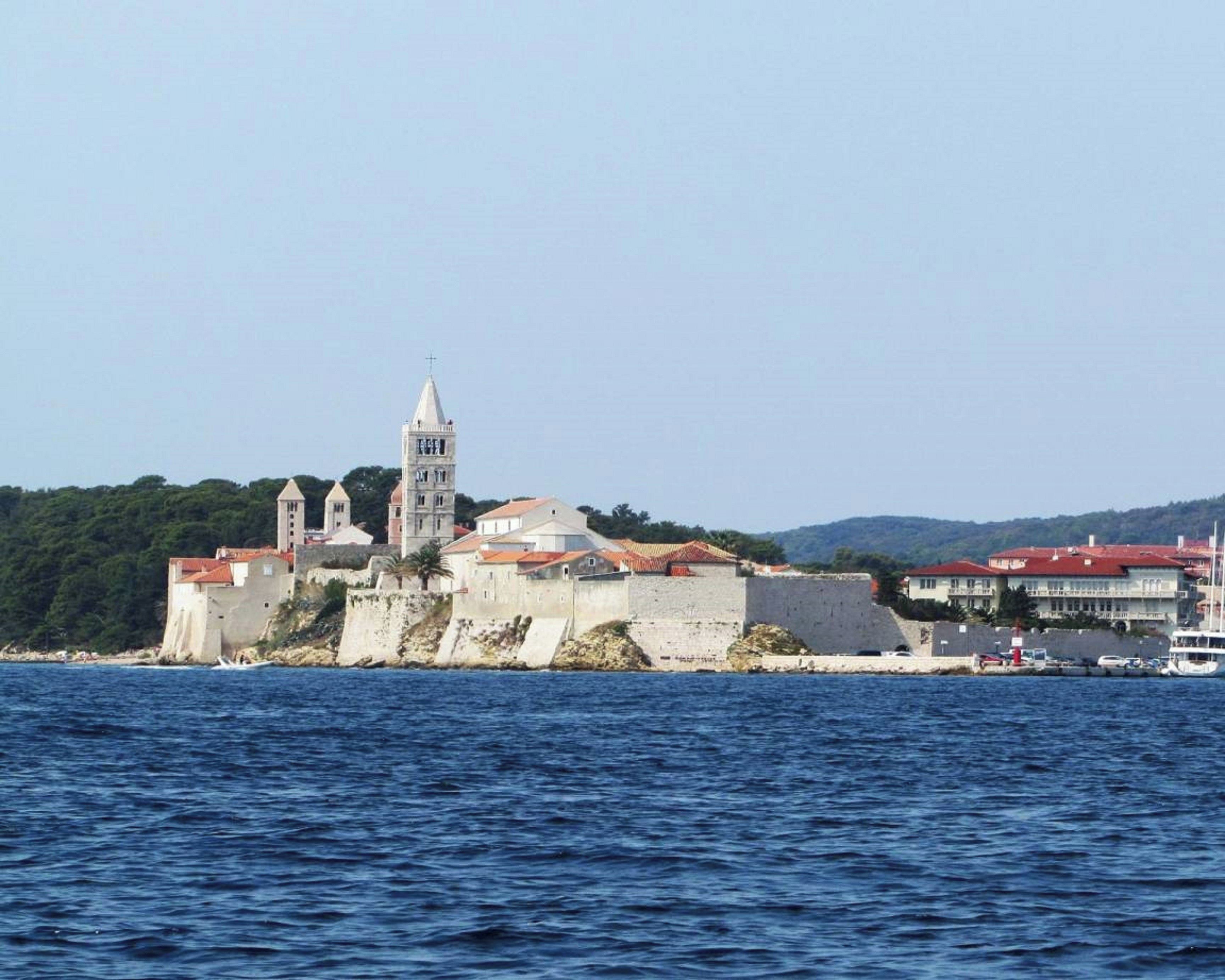 A coastal fortress with a prominent bell tower, surrounded by water and greenery.