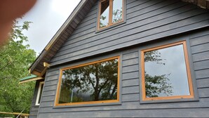 A house with a grey siding exterior, large windows with wooden frames, and a wooden deck. - Parque Nacional Conguillio, frente al Volcán, la mejor vista (Melipeuco)