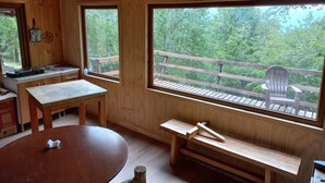 A wooden cabin interior with a large window, a wooden deck outside, and a table with a bench. - Parque Nacional Conguillio, frente al Volcán, la mejor vista (Melipeuco)