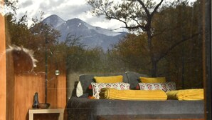 A bedroom with a bed, a small table, and a window overlooking a mountain. - Conguillio Park Cabin for 4 people (Melipeuco, Araucania)