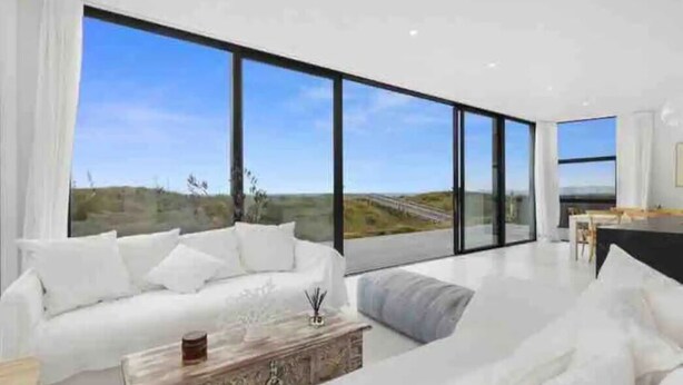 Una sala de estar moderna con un sofá blanco, una mesa de centro y ventanas amplias con vistas al paisaje.
