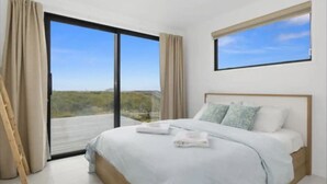 Un dormitorio moderno con una cama grande, vista a través de una puerta corredera de vidrio y una ventana con vista al cielo.
