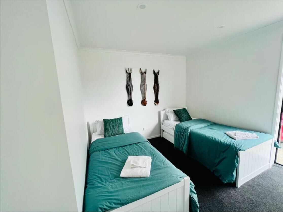 Une chambre avec deux lits, chacun recouvert d’une couverture verte et doté de draps blancs. Trois éléments décoratifs sont accrochés au mur au-dessus des lits.