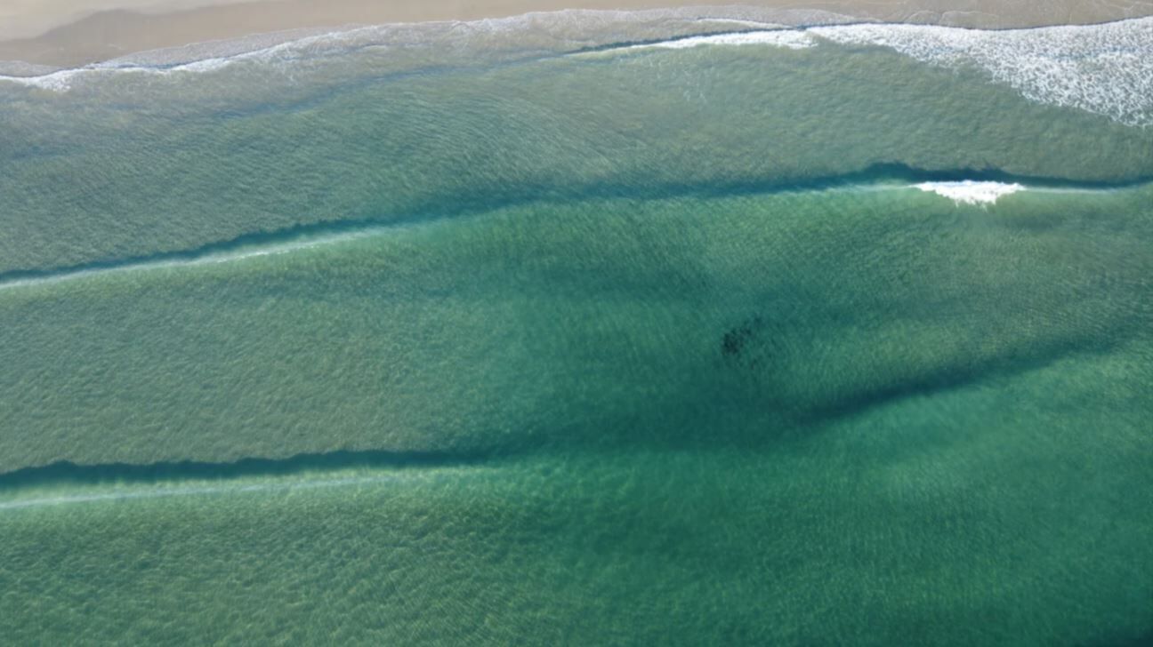 Luchtbeeld van een strand met helder turquoise water en een zandstrand.