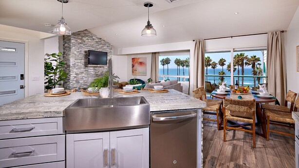 A modern kitchen with a stone backsplash, stainless steel appliances, and a dining area with a view of the ocean. - Oceanfront Gem: Dog-Friendly, AC, 2 Parking Spots, Walk to Pier & Shops (Oceanside)