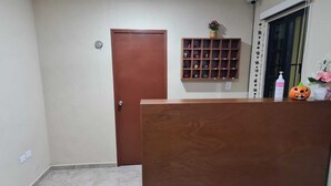 A room with a wooden reception desk, a door, a shelf with decorative items, and a window with a view. - Hotel La Piramide Izamal (Izamal)