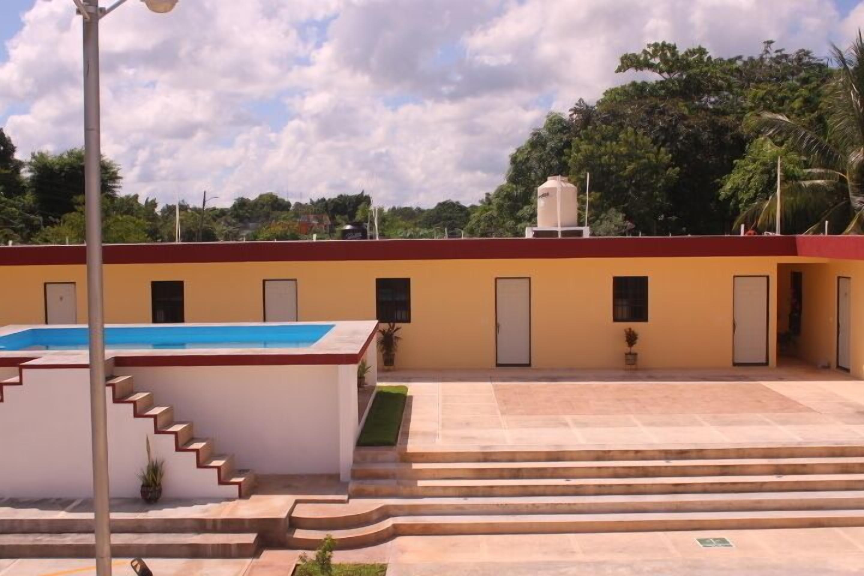 Un edificio con piscina, una escalera que lleva a la entrada y un tejado rojo.