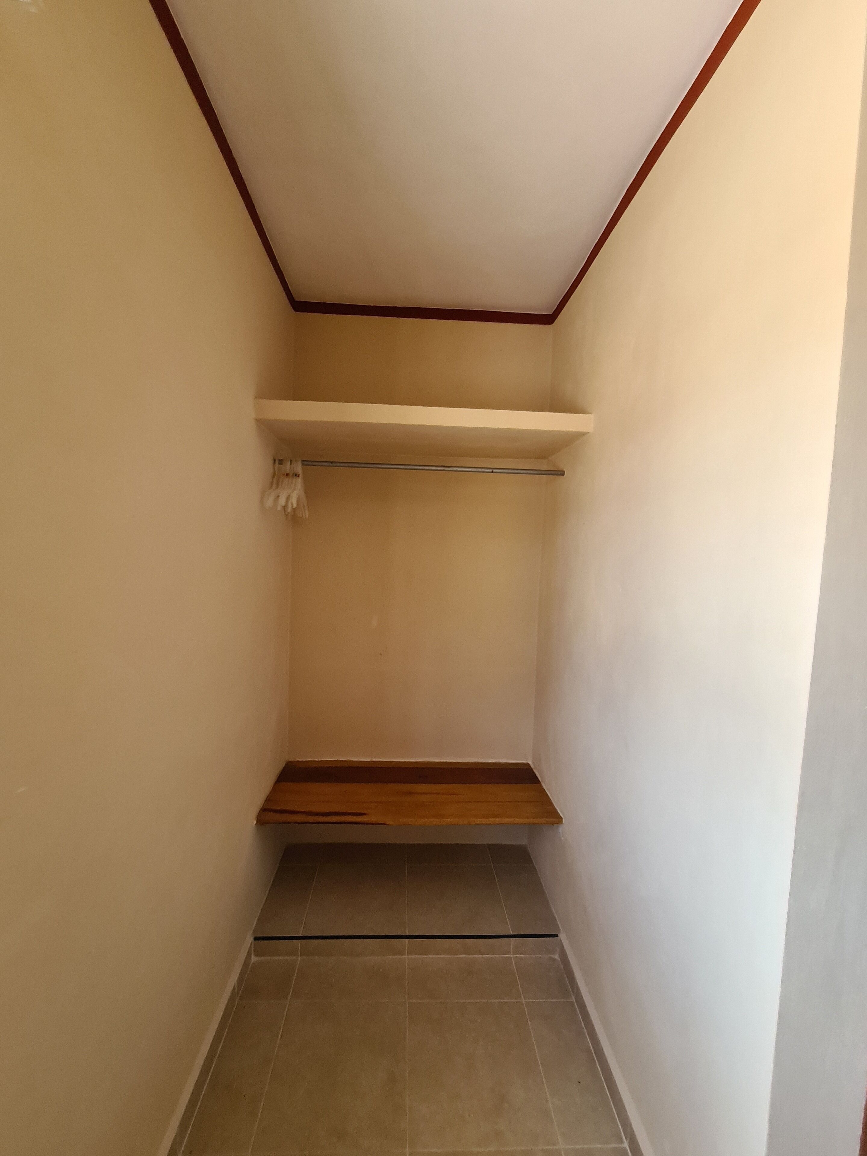 A narrow hallway with a wooden shelf and a towel rack on the wall.