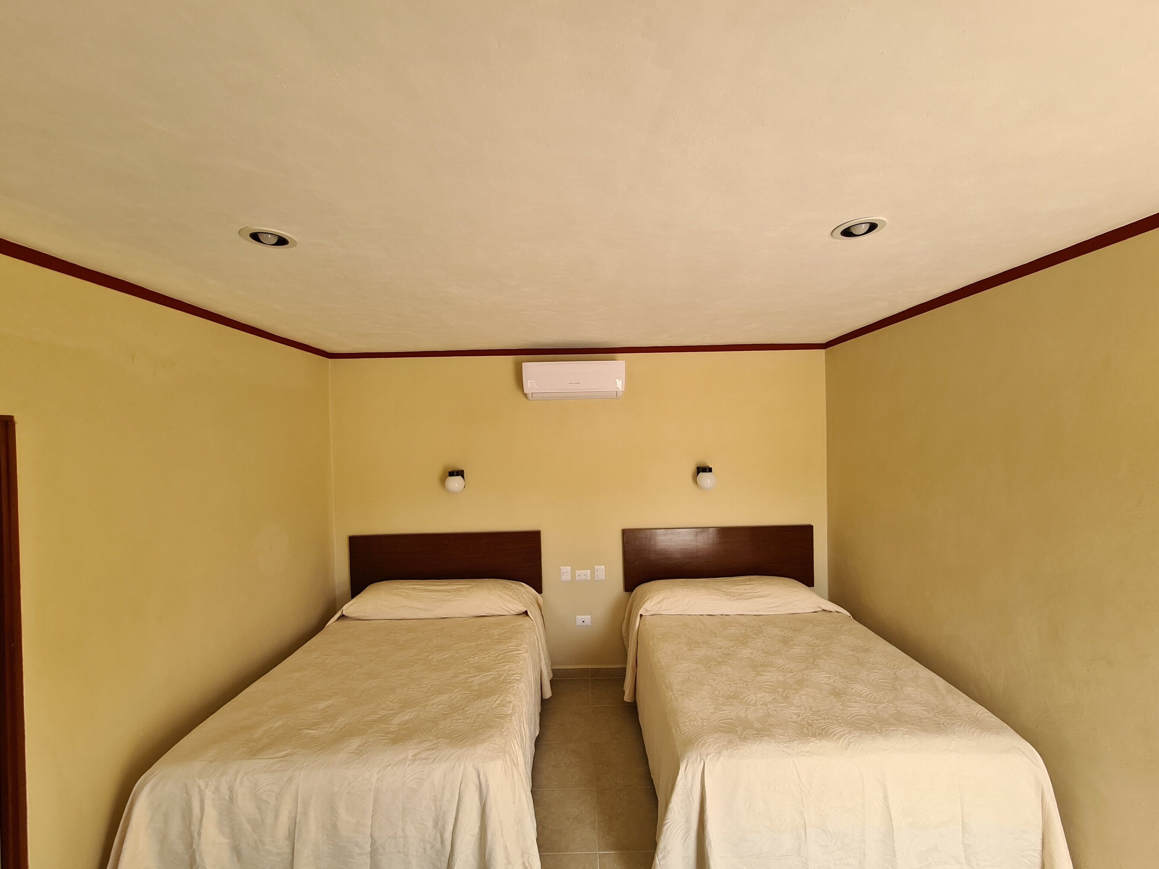 Una habitación de hotel con dos camas individuales, un ventilador de techo, un equipo de aire acondicionado y un ventanal.