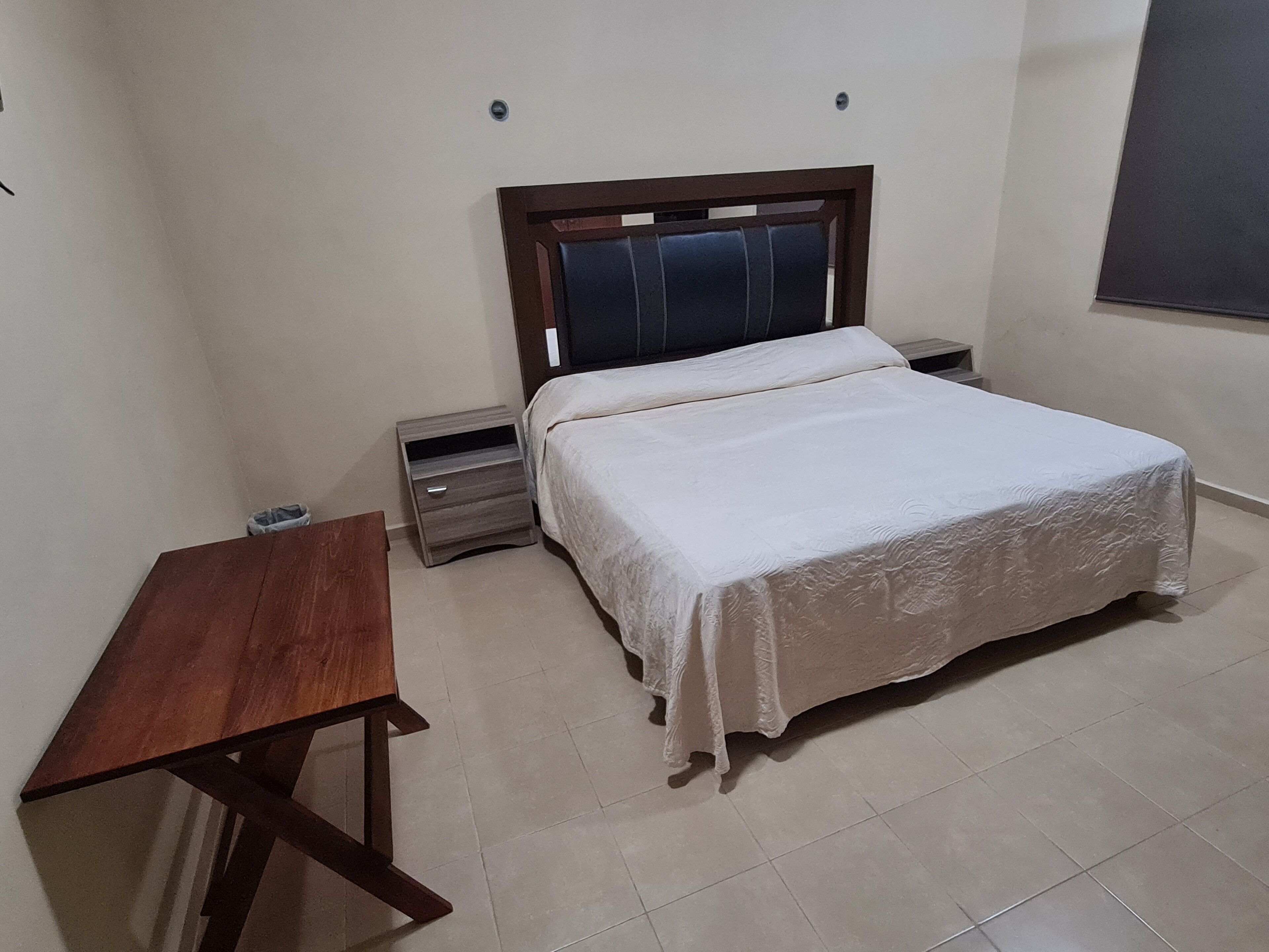 Ein Schlafzimmer mit einem Bett, einem Nachttisch, einem Holztisch und einem gefliesten Boden.