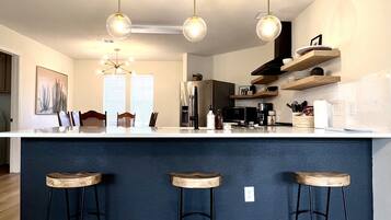 A modern kitchen with a central island, bar stools, pendant lighting, and a view of the adjacent living area.